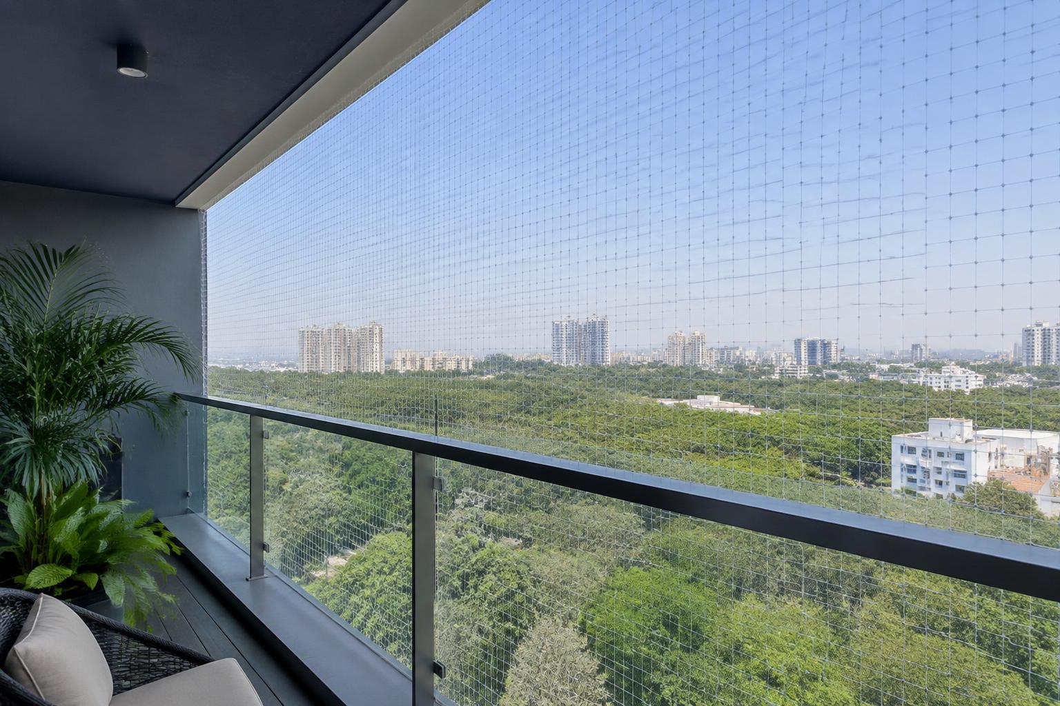 A contemporary high-rise balcony with fine, professionally installed transparent safety netting and a Hyderabad skyline